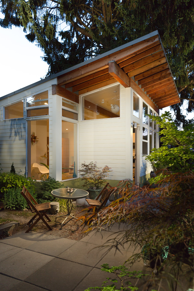 На фото: маленький, одноэтажный, белый дом в современном стиле с облицовкой из ЦСП и односкатной крышей для на участке и в саду с
