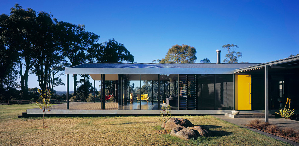 Immagine della facciata di una casa grande contemporanea a un piano con rivestimento in vetro e tetto a capanna