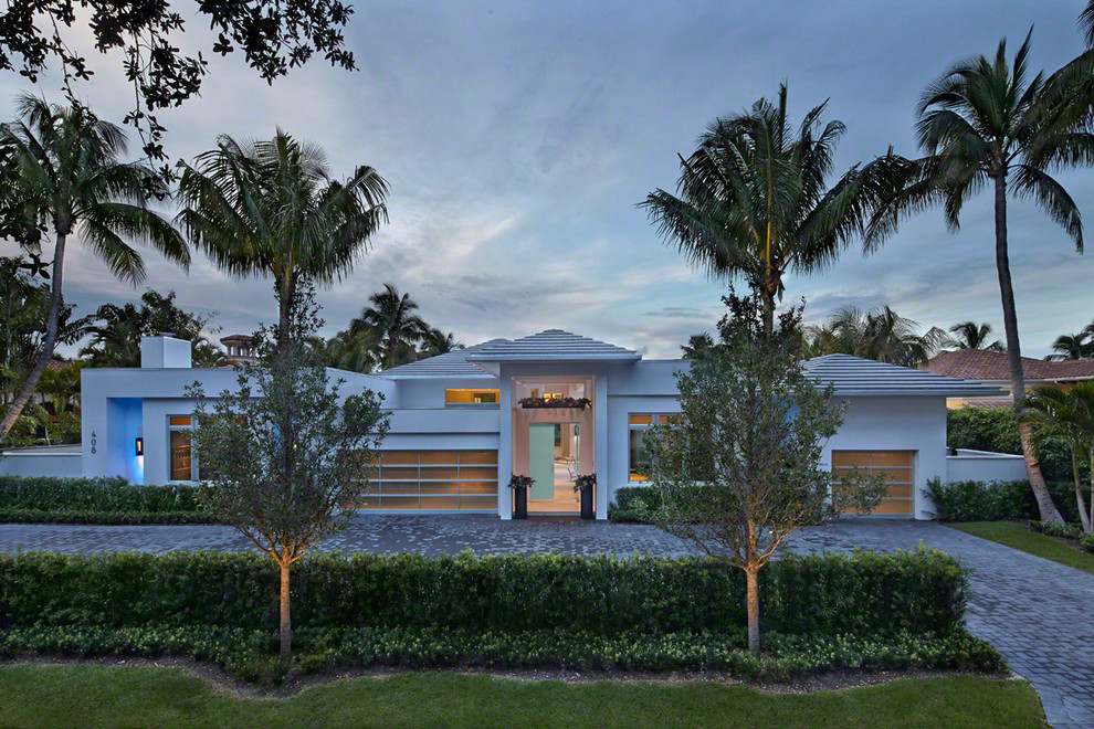 Large trendy white one-story stone exterior home photo in Miami with a hip roof