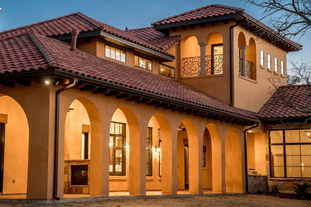 Modelo de fachada de casa beige mediterránea grande de dos plantas con revestimiento de adobe, tejado a cuatro aguas y tejado de teja de barro