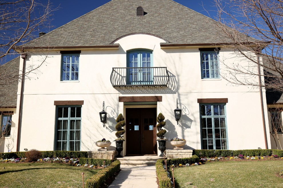 Cette image montre une grande façade de maison beige traditionnelle en stuc à un étage avec un toit à quatre pans.