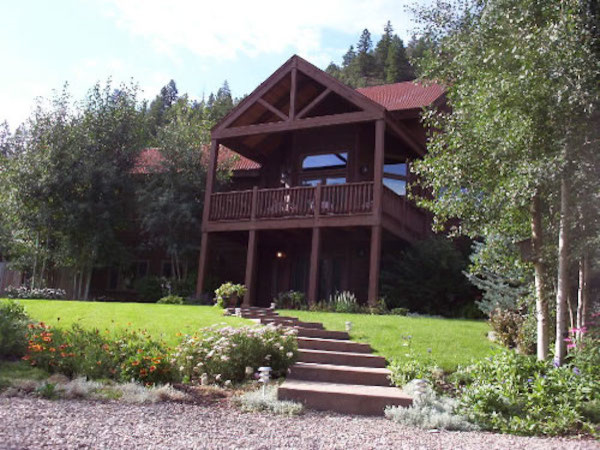 Esempio della villa grande marrone rustica a due piani con rivestimento in legno, tetto a capanna e copertura in tegole
