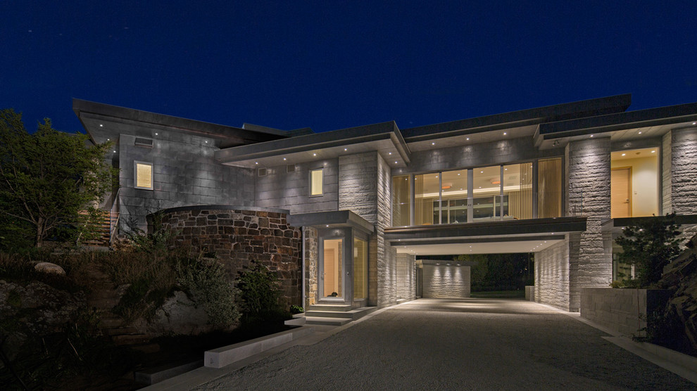 Пример оригинального дизайна: огромный, двухэтажный, серый частный загородный дом в современном стиле с облицовкой из камня и плоской крышей