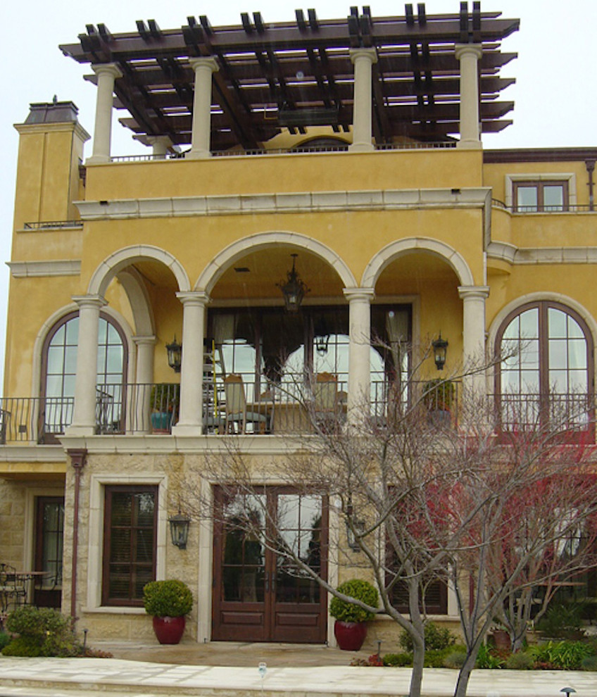 Imagen de fachada amarilla mediterránea extra grande de tres plantas con revestimiento de estuco y tejado a dos aguas