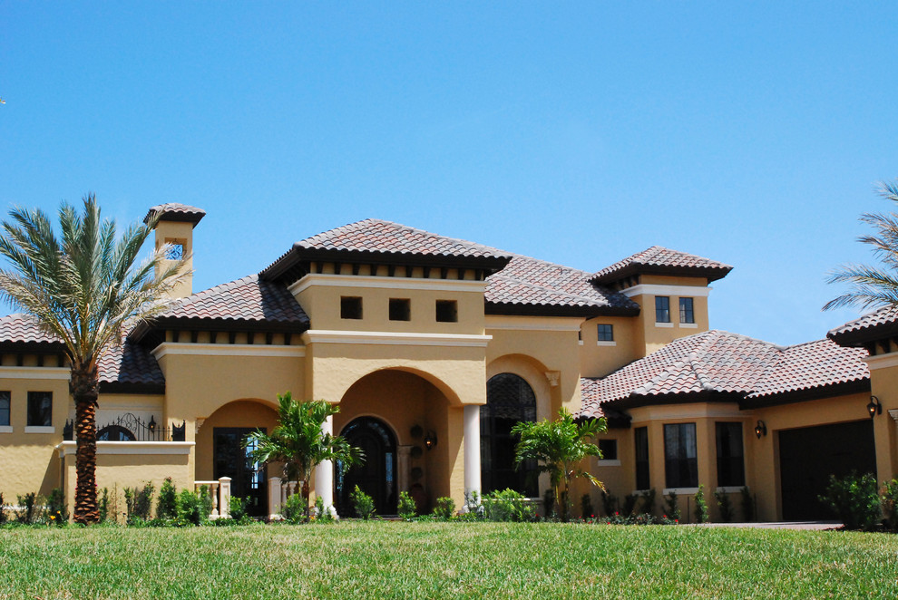 Пример оригинального дизайна: большой, двухэтажный, бежевый дом в средиземноморском стиле с облицовкой из цементной штукатурки и вальмовой крышей