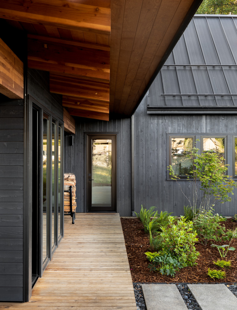 Cette image montre une grande façade de maison noire chalet en bois de plain-pied avec un toit en appentis et un toit en métal.