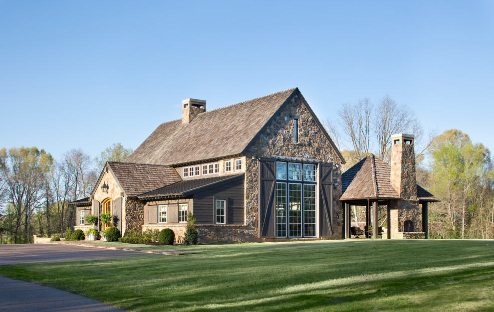 Идея дизайна: большой, трехэтажный, коричневый частный загородный дом в стиле кантри с облицовкой из камня, двускатной крышей и крышей из гибкой черепицы