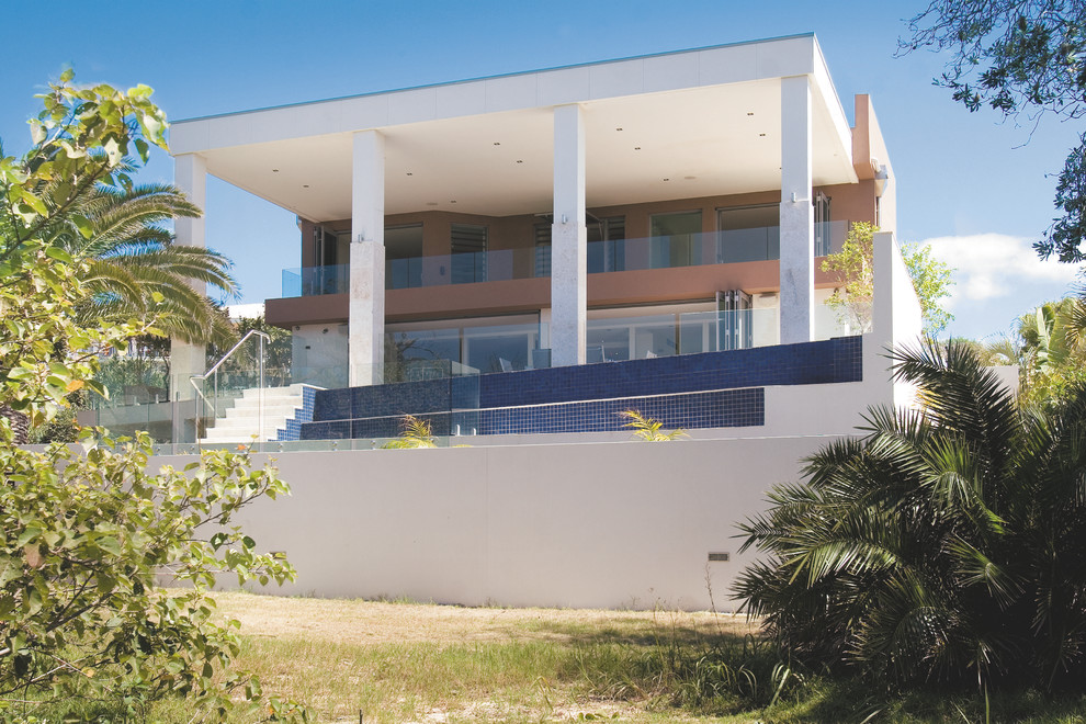 Large and beige modern concrete house exterior in Sunshine Coast with three floors and a flat roof.