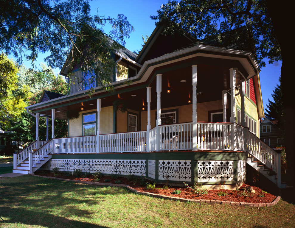 Imagen de fachada de casa amarilla y azul tradicional grande de dos plantas con revestimiento de madera, tejado a dos aguas, tejado de teja de madera, escaleras y tablilla