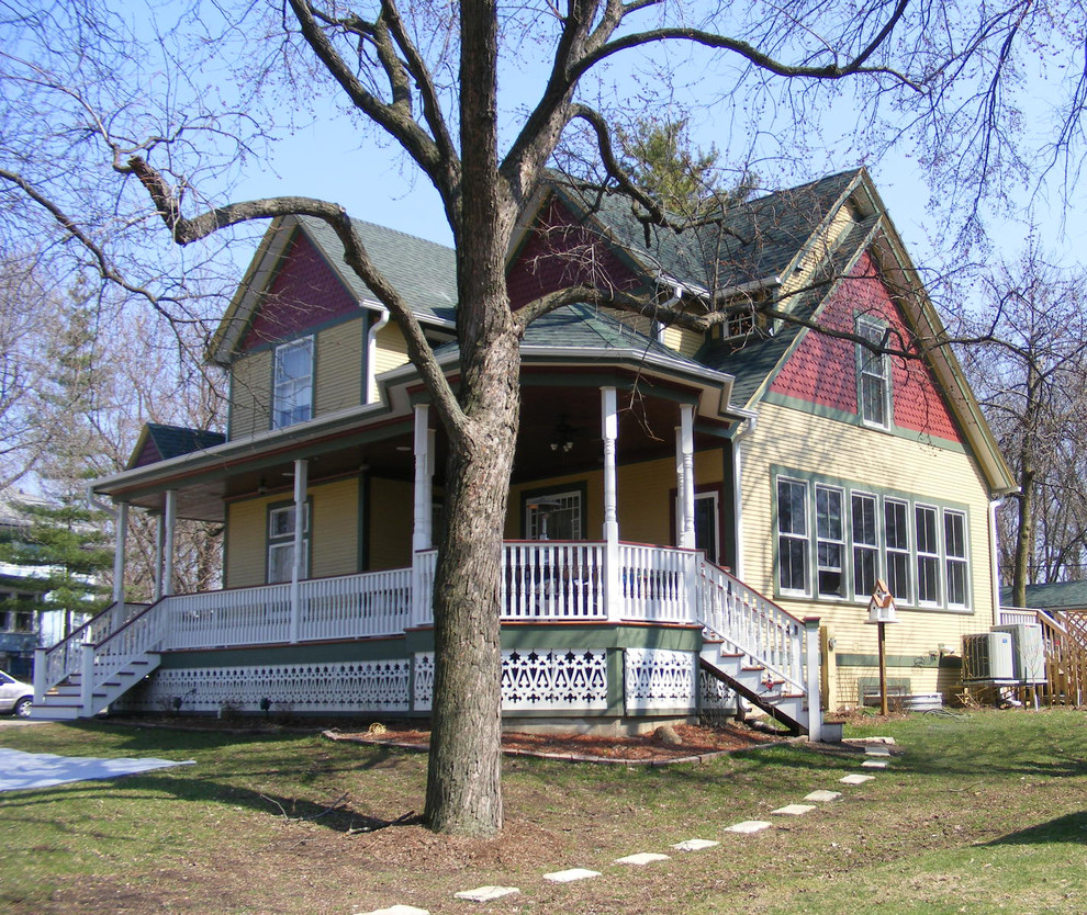 Пример оригинального дизайна: двухэтажный, желтый, большой частный загородный дом в викторианском стиле с облицовкой из винила, двускатной крышей, крышей из гибкой черепицы, отделкой планкеном и синей крышей