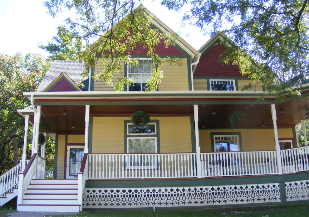 На фото: двухэтажный, желтый, большой частный загородный дом в викторианском стиле с облицовкой из винила, двускатной крышей, крышей из гибкой черепицы, отделкой планкеном и синей крышей
