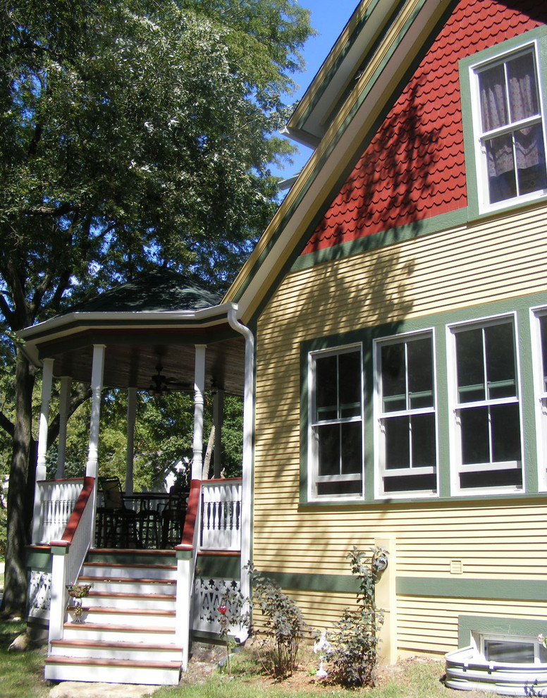 シカゴにある高級なヴィクトリアン調のおしゃれな家の外観 (ビニールサイディング、黄色い外壁、ウッドシングル張り) の写真