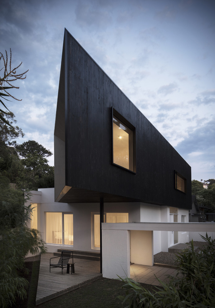 Medium sized and black modern two floor detached house in Sydney with wood cladding, a flat roof and a metal roof.