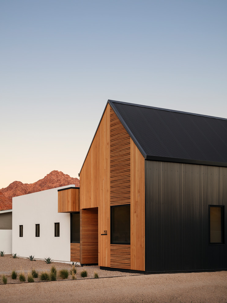 Imagen de fachada de casa moderna de una planta con revestimiento de madera, tejado a dos aguas y tejado de metal