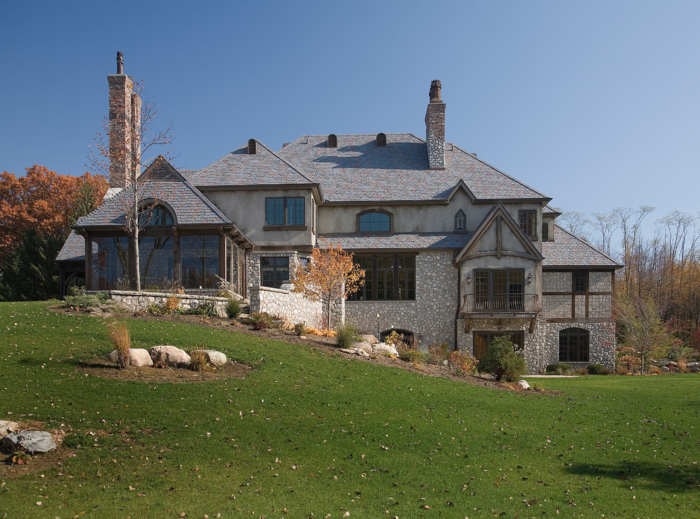 Пример оригинального дизайна: огромный, трехэтажный, бежевый частный загородный дом в классическом стиле с облицовкой из камня и крышей из смешанных материалов