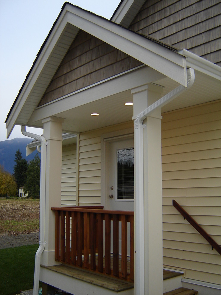 Foto della villa piccola gialla country a un piano con rivestimento in vinile, tetto a capanna e copertura a scandole