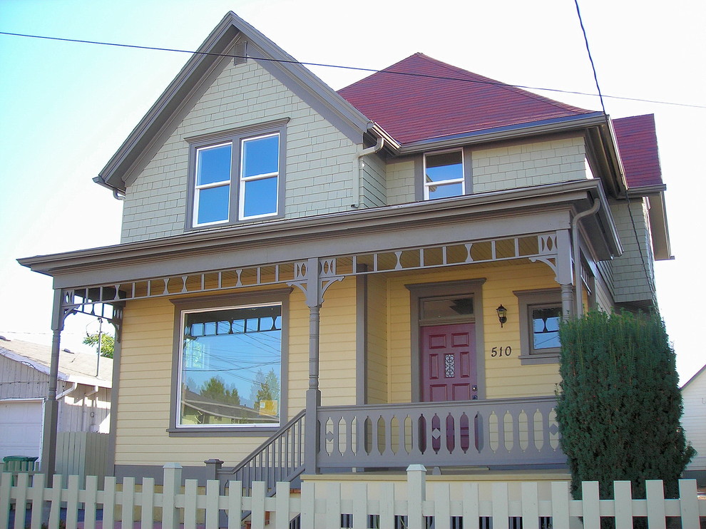 Foto della facciata di una casa ampia gialla vittoriana a due piani con rivestimento in legno e tetto a capanna