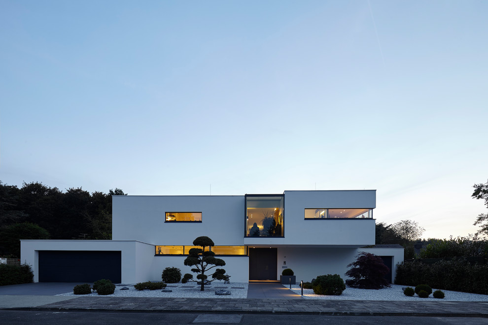 Пример оригинального дизайна: двухэтажный, белый частный загородный дом среднего размера в стиле модернизм с облицовкой из цементной штукатурки и плоской крышей