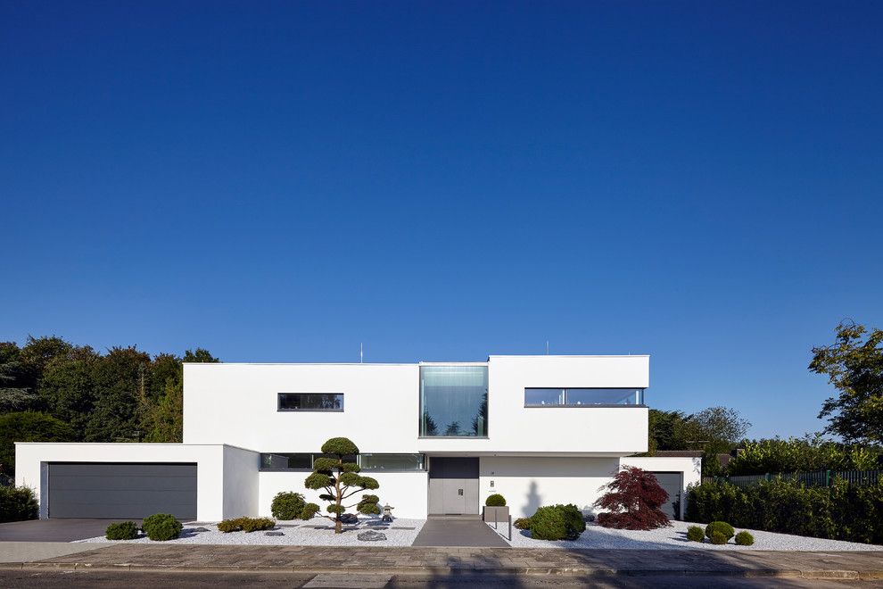 Пример оригинального дизайна: двухэтажный, белый частный загородный дом среднего размера в стиле модернизм с облицовкой из цементной штукатурки и плоской крышей