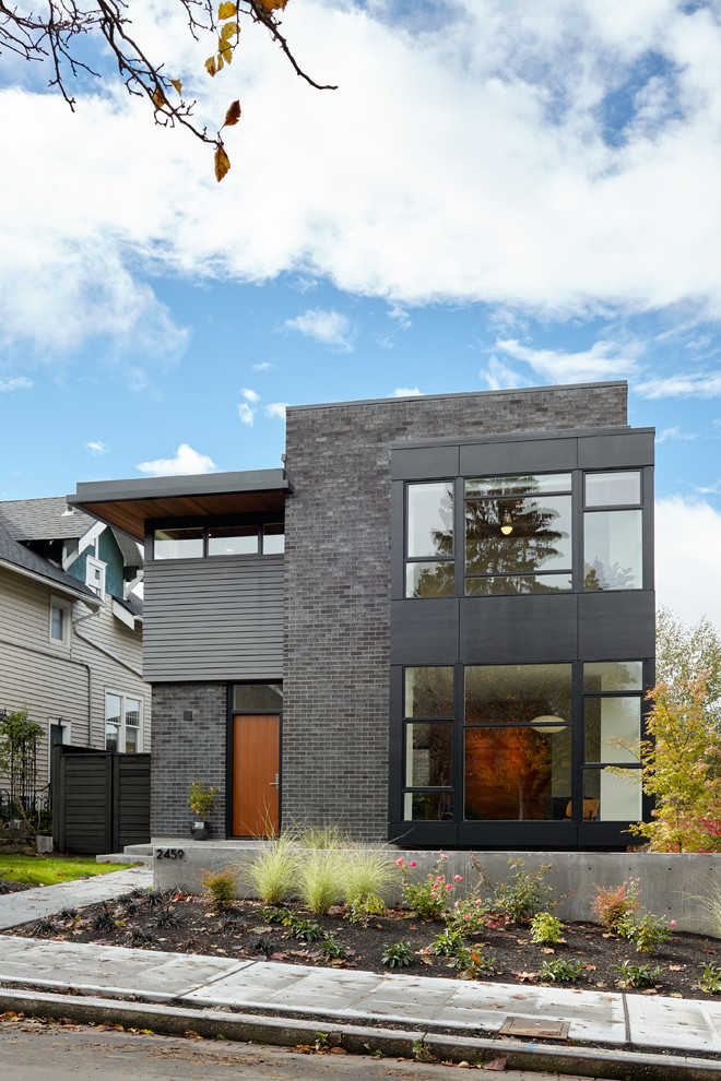 This is an example of a small and black modern brick house exterior in Seattle with three floors and a flat roof.