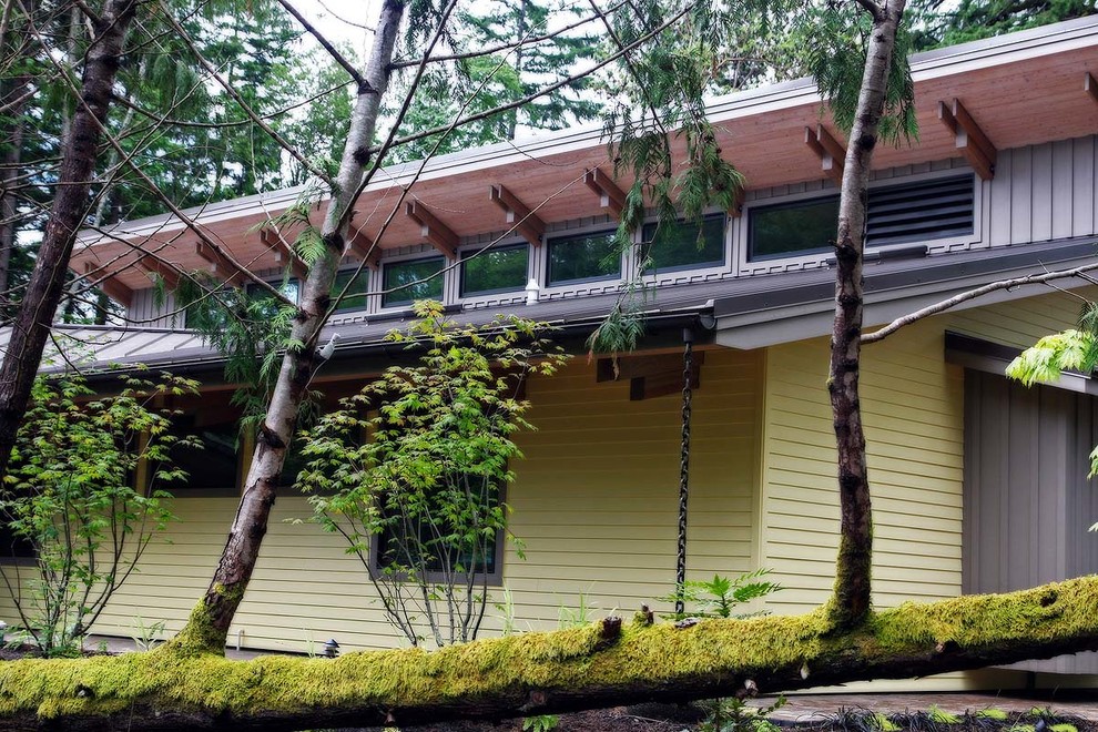 Modelo de fachada de casa amarilla contemporánea de tamaño medio de una planta con revestimiento de madera, tejado a doble faldón y tejado de metal