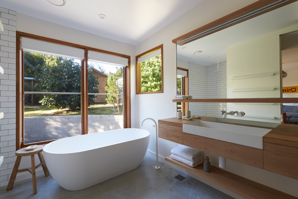 Medium sized contemporary ensuite bathroom in Other with flat-panel cabinets, medium wood cabinets, a freestanding bath, metro tiles, white walls, concrete flooring, a built-in sink, wooden worktops and brown worktops.