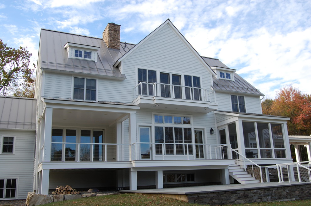 Foto della facciata di una casa ampia bianca classica a tre piani con rivestimento con lastre in cemento e falda a timpano