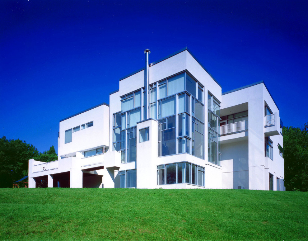 Immagine della villa grande bianca moderna a tre piani con rivestimenti misti, tetto piano e terreno in pendenza