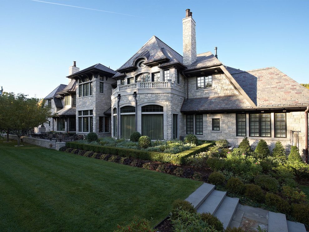 Imagen de fachada de casa gris tradicional extra grande de dos plantas con revestimiento de piedra, tejado a cuatro aguas y tejado de teja de madera