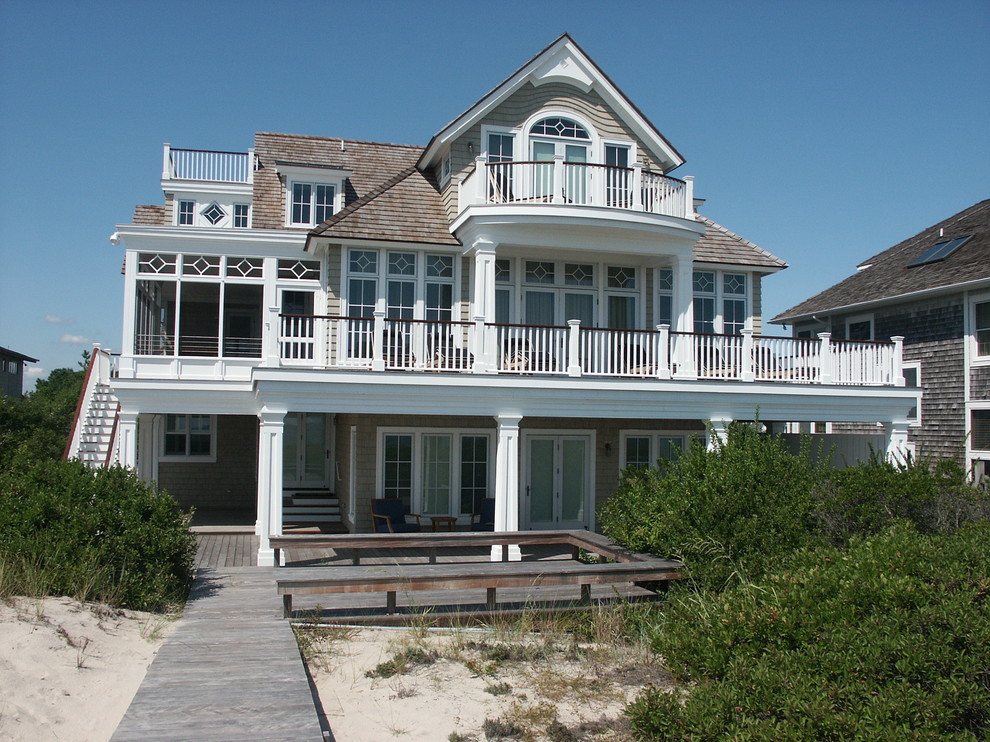 Large and beige coastal house exterior in Other with three floors, vinyl cladding, a hip roof, a shingle roof and a brown roof.