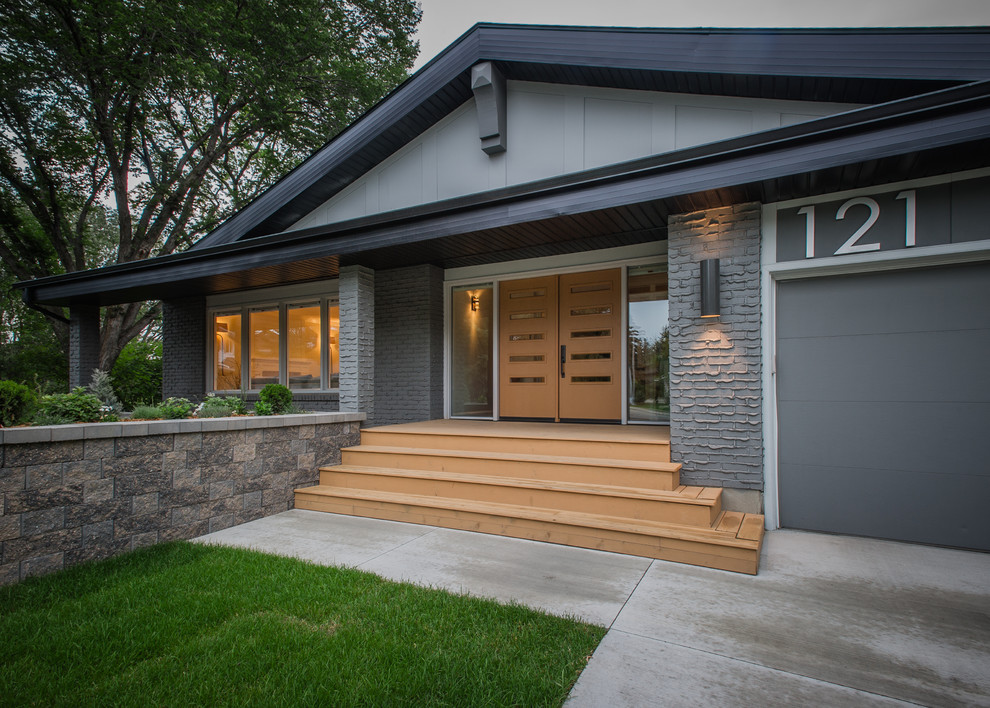 На фото: кирпичный, серый дом среднего размера в стиле фьюжн с разными уровнями и двускатной крышей
