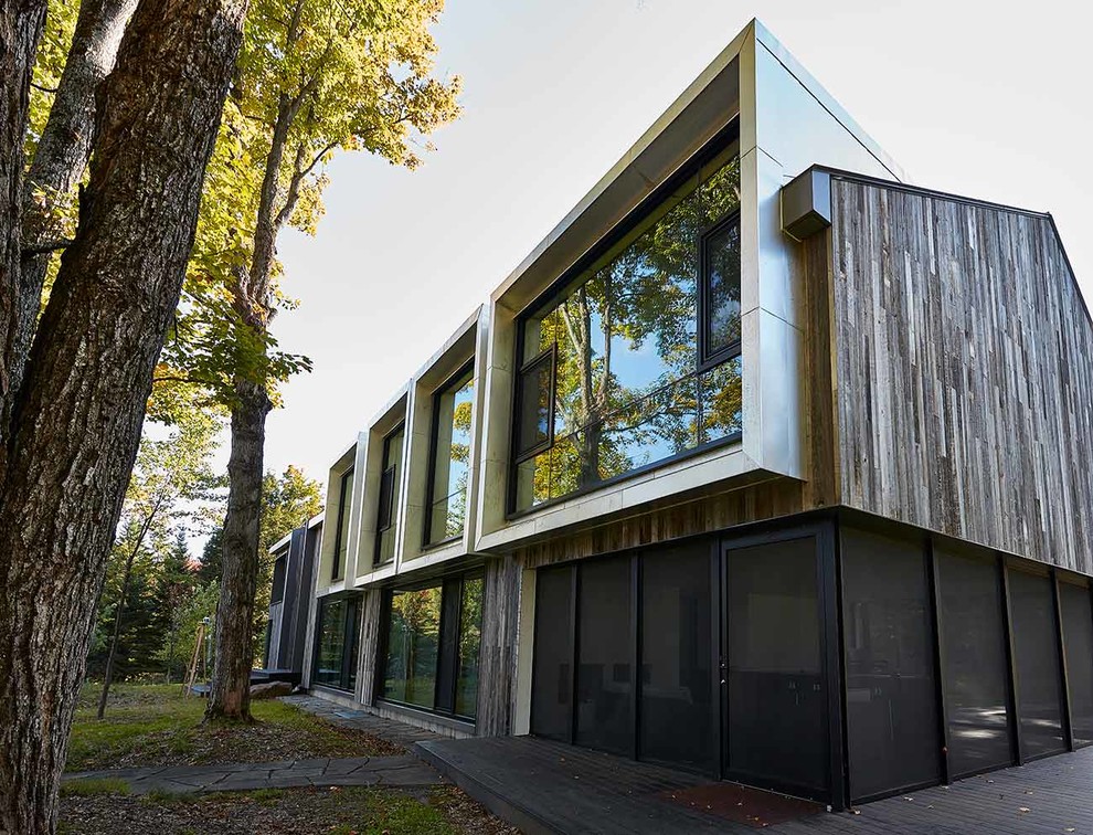 Medium sized and gey contemporary two floor detached house in Montreal with wood cladding, a half-hip roof and a metal roof.