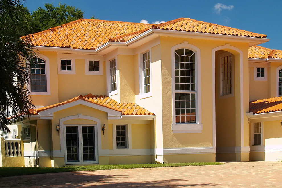 Immagine della villa gialla mediterranea a due piani di medie dimensioni con rivestimento in stucco, tetto a padiglione e copertura in tegole