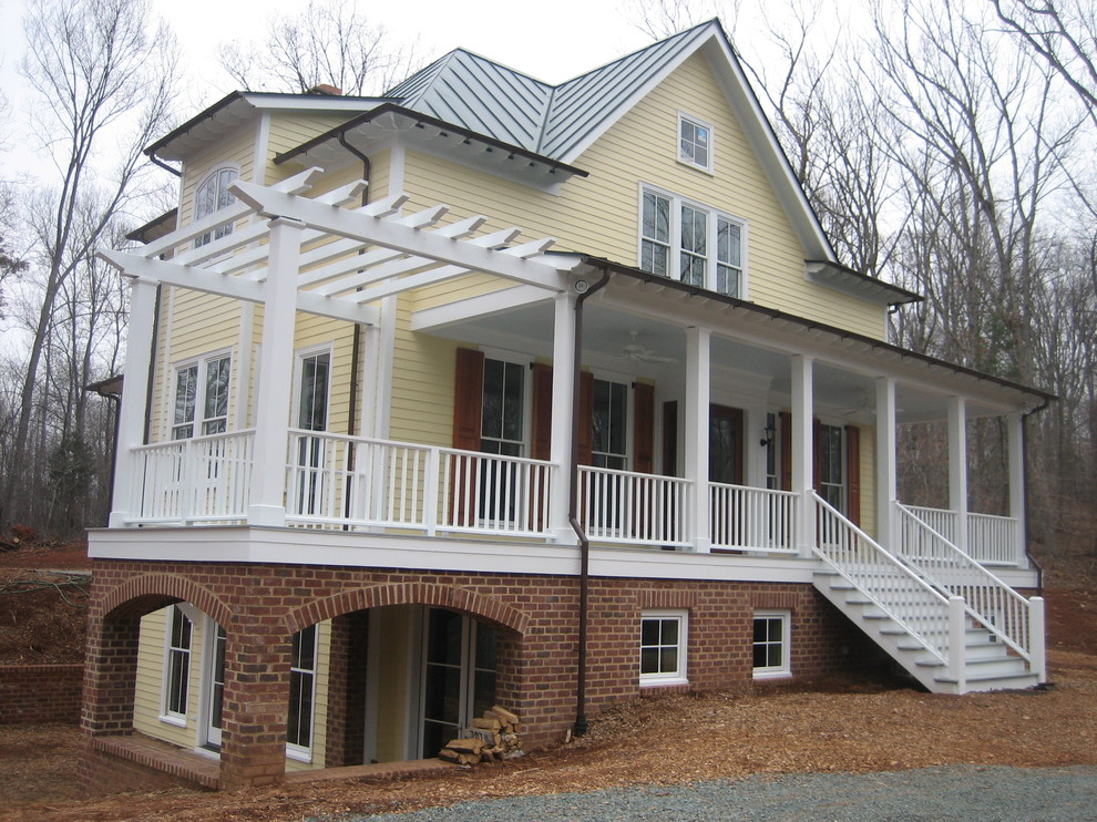 Réalisation d'une façade de maison jaune tradition à deux étages et plus et de taille moyenne avec un toit à quatre pans, un revêtement en vinyle et un toit en métal.