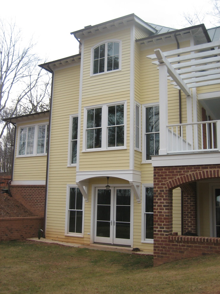 Cette image montre une façade de maison jaune traditionnelle en panneau de béton fibré à deux étages et plus avec un toit à quatre pans.