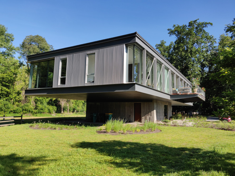 Foto på ett mellanstort funkis grått hus, med två våningar, metallfasad, platt tak och tak i mixade material