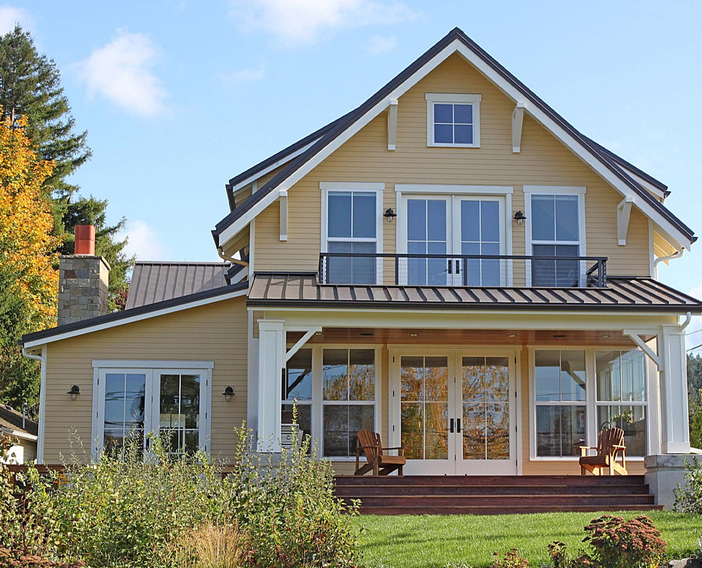 Foto della facciata di una casa grande gialla country a tre piani con rivestimento in legno e tetto a capanna