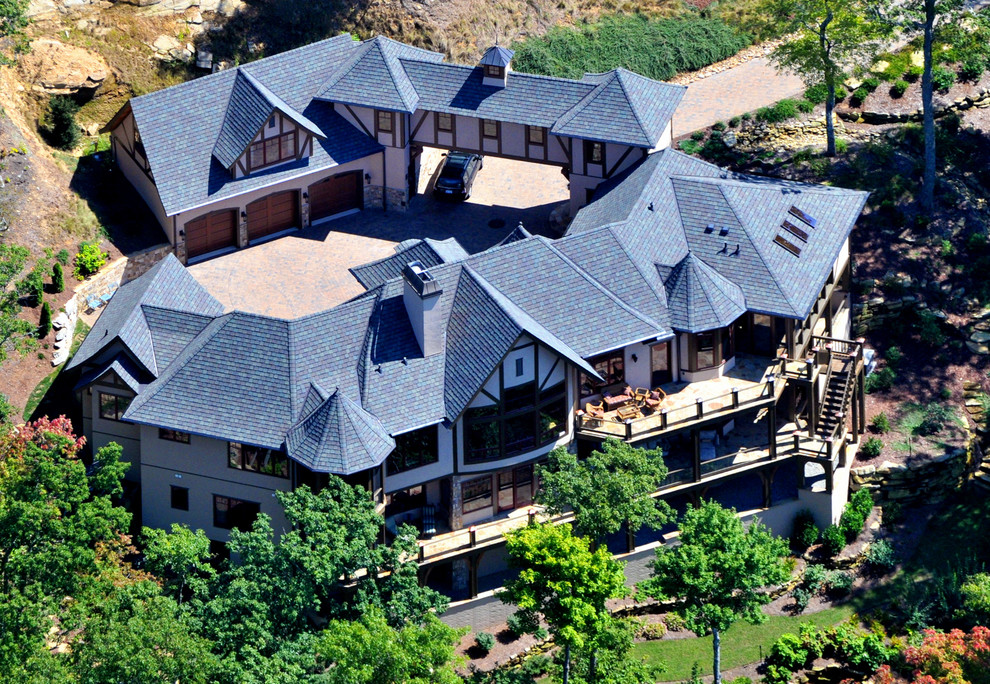 На фото: огромный, трехэтажный, бежевый частный загородный дом в классическом стиле с облицовкой из цементной штукатурки, вальмовой крышей, крышей из гибкой черепицы и коричневой крышей с
