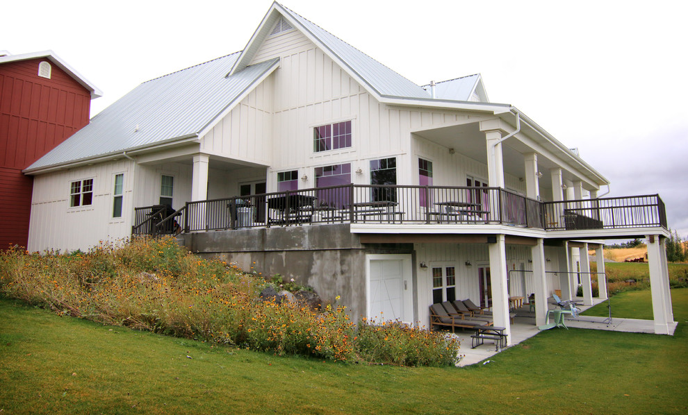 Immagine della villa grande bianca country a due piani con rivestimento in legno, tetto a capanna e copertura in metallo o lamiera