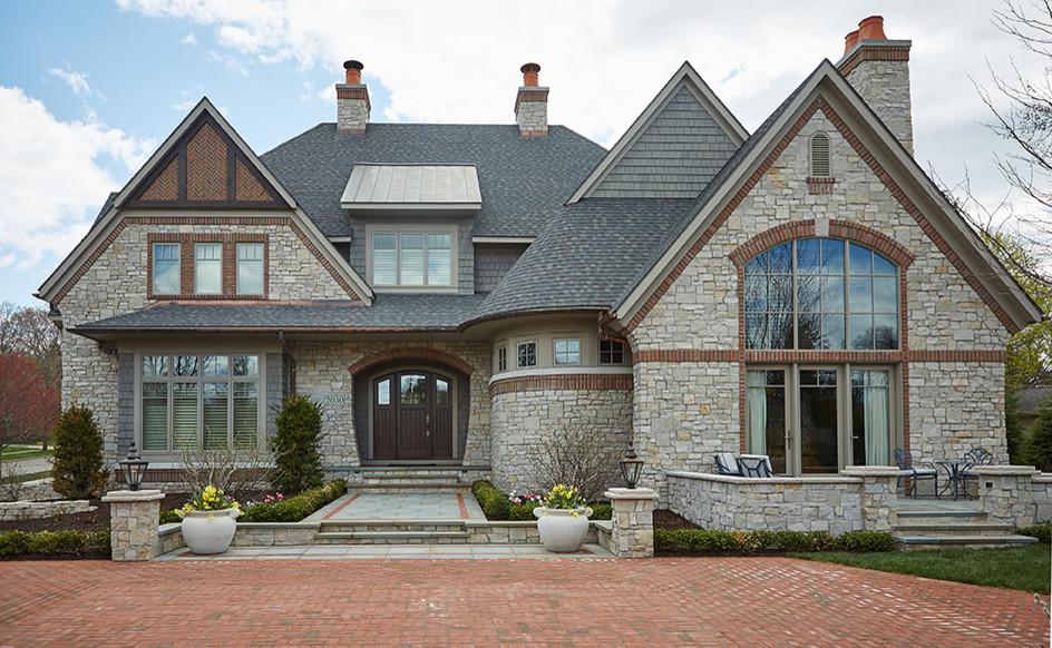 Diseño de fachada de casa gris clásica extra grande de tres plantas con revestimiento de piedra, tejado de varios materiales y tejado a dos aguas