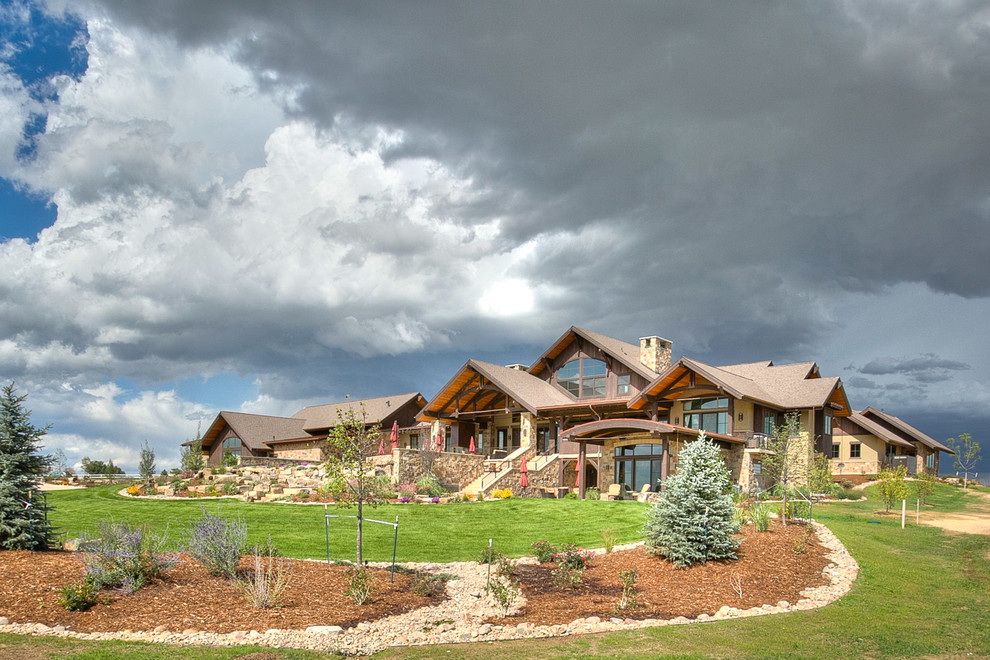 Example of a huge mountain style beige two-story stone gable roof design in Denver