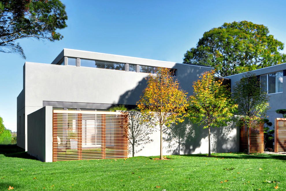 Idée de décoration pour une grande façade de maison grise minimaliste en stuc à un étage avec un toit plat.