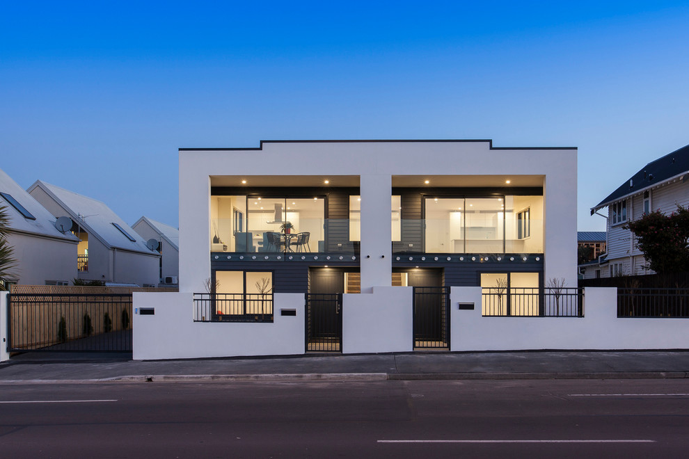 Small modern white two-story stucco exterior home idea in Christchurch with a metal roof and a black roof