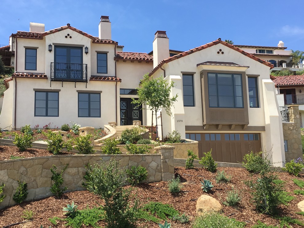 Example of a large tuscan beige three-story stucco house exterior design in Santa Barbara with a clipped gable roof and a tile roof