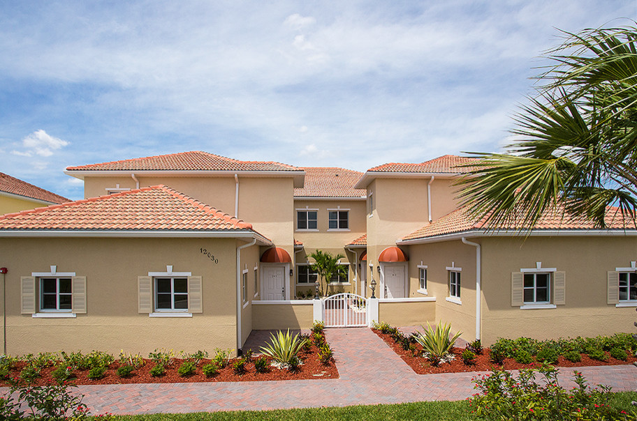 Modelo de fachada de casa bifamiliar beige costera grande de dos plantas con revestimiento de estuco, tejado a cuatro aguas y tejado de teja de barro