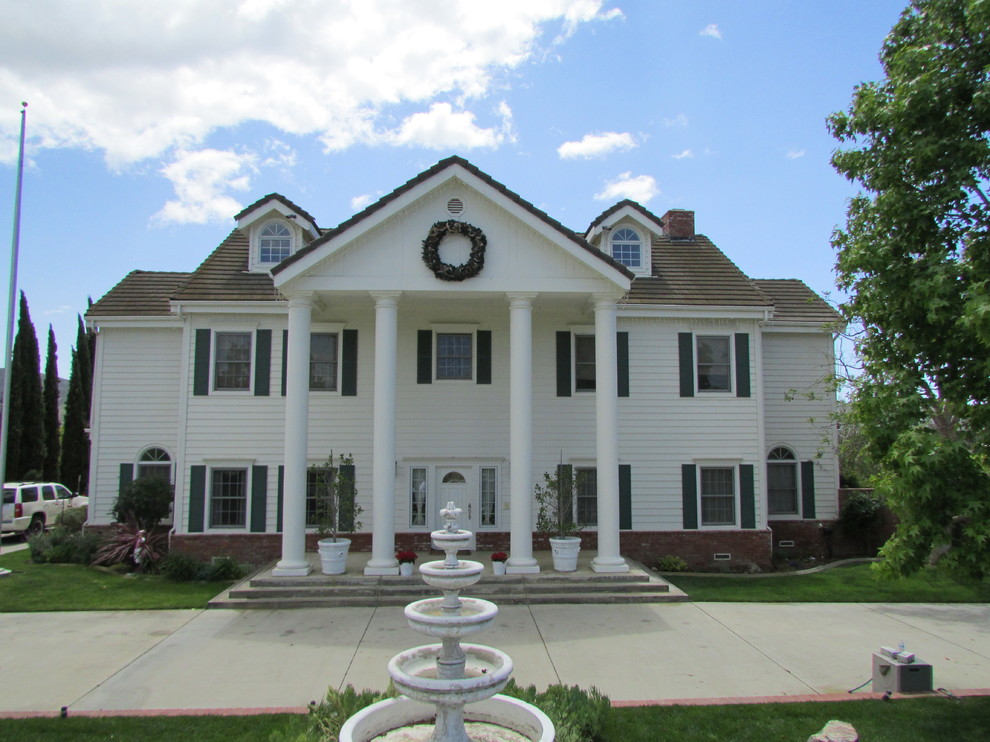 Foto della facciata di una casa grande bianca classica a due piani con rivestimento con lastre in cemento e tetto a capanna
