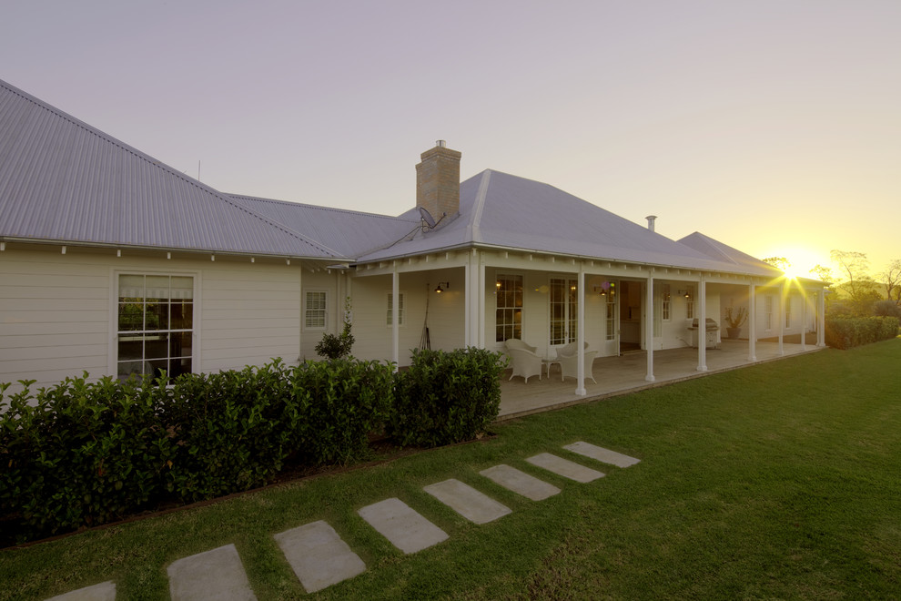 Photo of a large and white rural bungalow house exterior in Sydney with wood cladding and a hip roof.