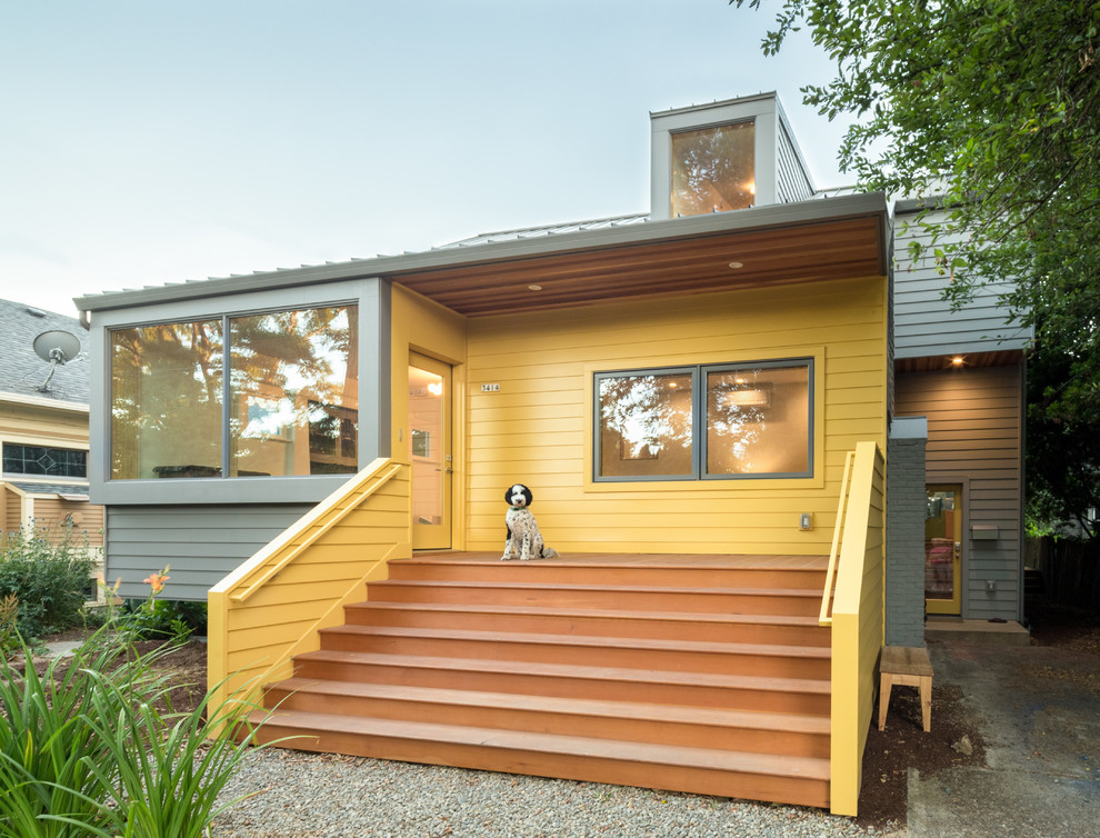 Cette photo montre une façade de maison jaune rétro à un étage avec un toit en métal.