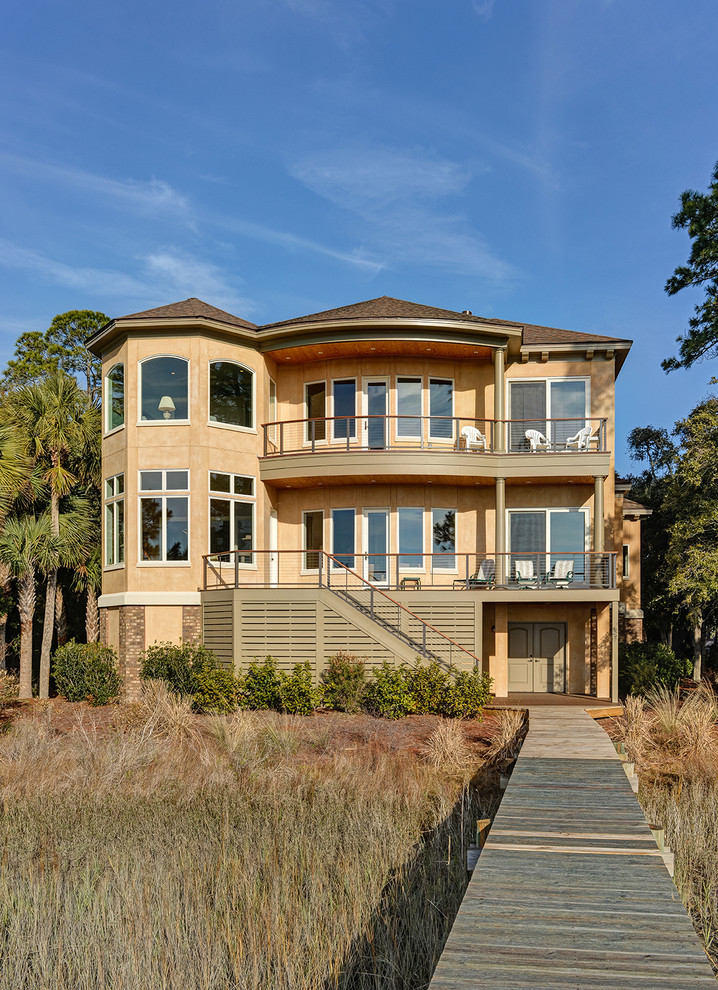 Example of a large classic beige three-story stucco house exterior design in Charleston with a hip roof, a shingle roof and a brown roof