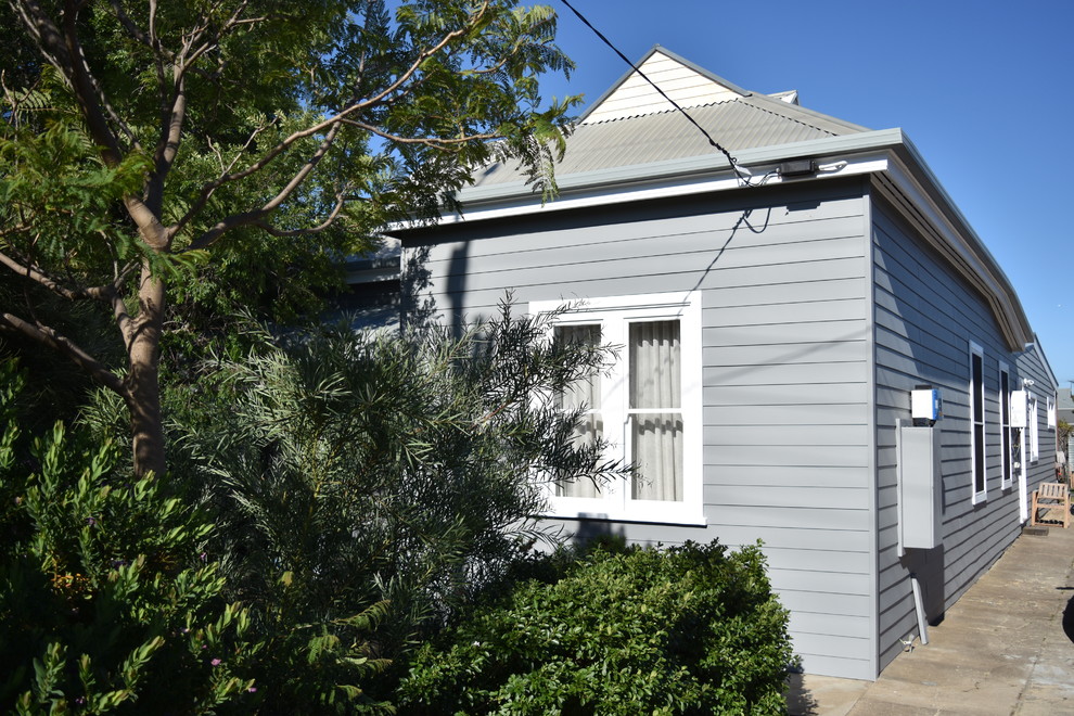 Imagen de fachada de casa gris de tamaño medio de una planta con revestimiento de aglomerado de cemento, tejado a dos aguas y tejado de metal